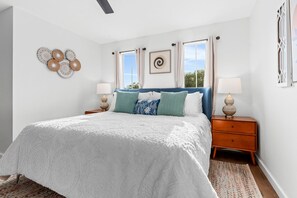 A bedroom with a large bed, two bedside tables, a window with curtains, and wall decor. - Casa Blanco (Wimberley)
