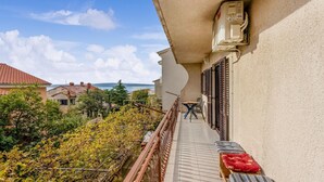 A balcony with a view of the sea, a table with chairs, and a red cushion.