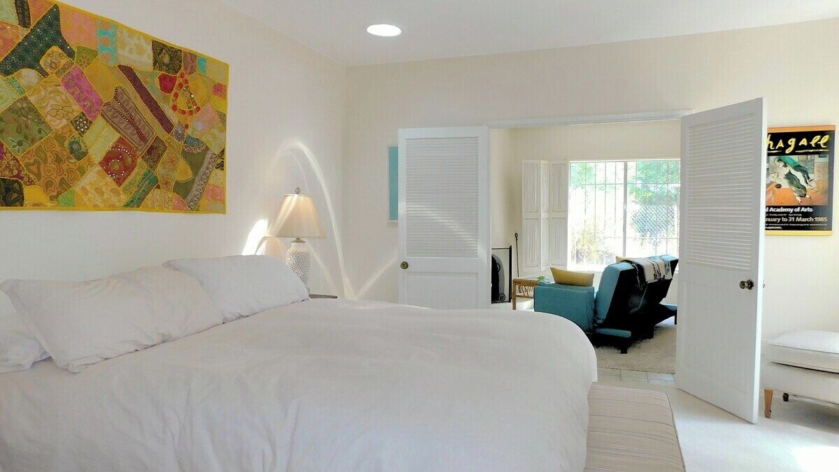 Ein Hotelzimmer mit einem großen Bett, einem farbenfrohen Kunstwerk an der Wand, einer Tür zu einem Balkon und einem Poster an der Wand.