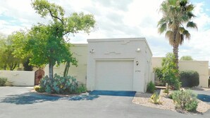 A single-story building with a garage door, surrounded by desert vegetation including cacti and a palm tree. - Avenida San Valle, Sabino Canyon (Tucson)