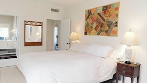 A bedroom with a large bed, two bedside lamps, a mirror, and a colorful quilt on the wall. - Avenida San Valle, Sabino Canyon (Tucson)