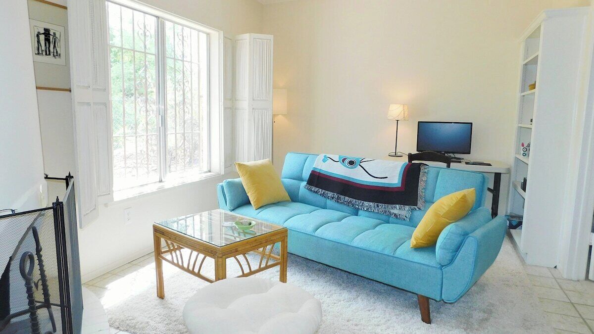 Een woonkamer met een blauwe bank, een glazen salontafel, een witte fauteuil, een televisie en een boekenkast.