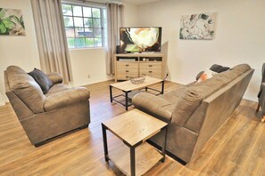 A living room with two sofas, a coffee table, a TV on a wooden stand, and a window with curtains. - Eclectic Oasis on Brown, Pet Friendly (Tucson)