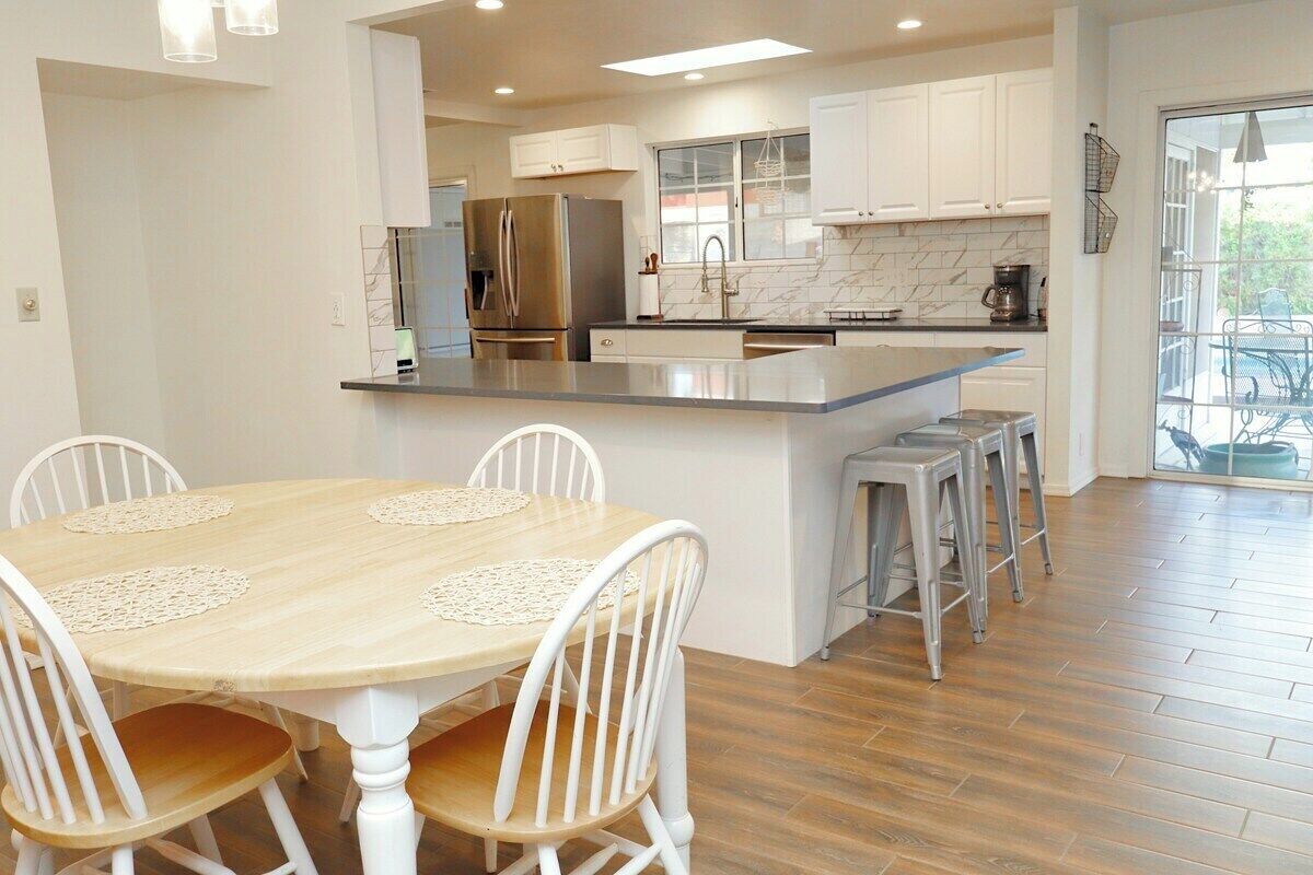 A modern kitchen with white cabinetry, a stainless steel refrigerator, and a large island with stools.