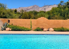 En swimmingpool med kristallklart blått vatten, omgiven av ett ökenlandskap med berg i bakgrunden.
