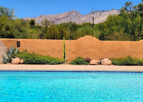 A swimming pool with clear blue water, surrounded by a desert landscape with mountains in the background.