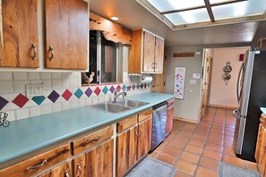 Une cuisine avec des meubles de rangement en bois, un plan de travail bleu, un lave-vaisselle et un sol carrelé.