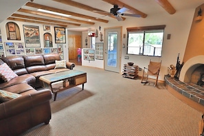 A living room with a brown leather sofa, a wooden coffee table, and a fireplace. There are framed pictures on the walls and a ceiling fan.