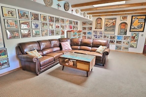 A room with a brown leather sectional sofa, a coffee table, and a wall adorned with framed posters.