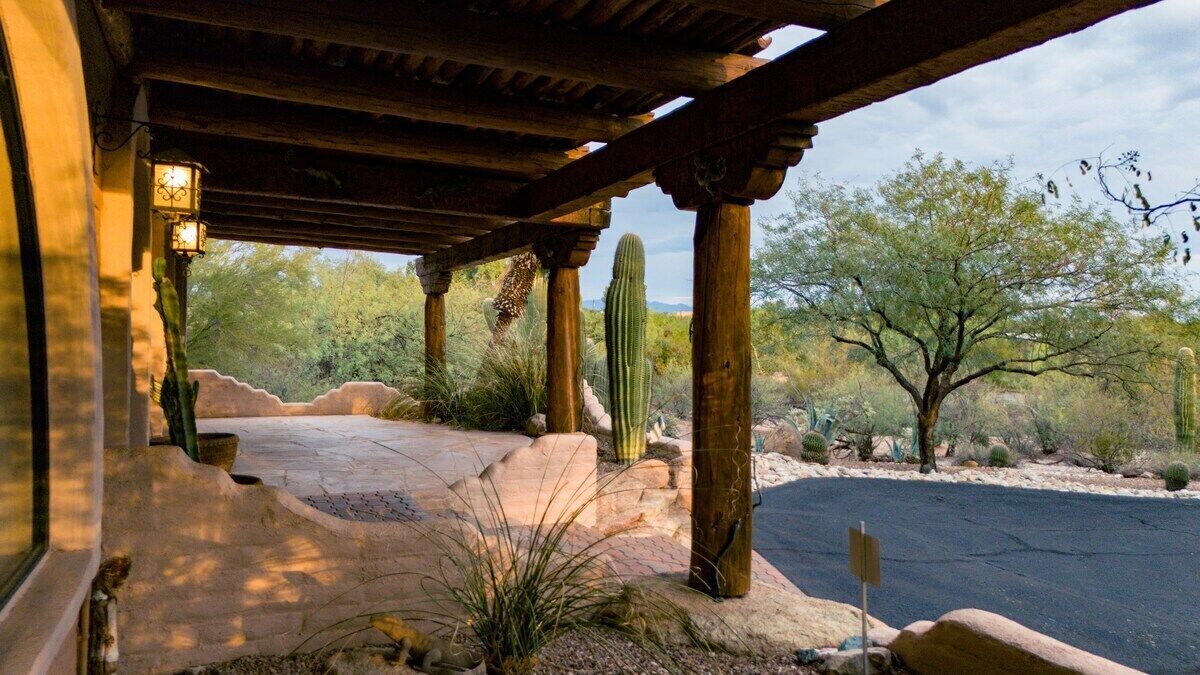 A covered outdoor area with a paved walkway, wooden columns, and cacti.