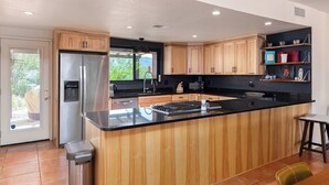 A modern kitchen with wooden cabinets, a stainless steel refrigerator, and a black countertop island. - Foothills Beauty with Pool and Mountain Views (Tucson)