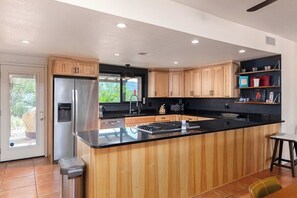A modern kitchen with wooden cabinets, a stainless steel refrigerator, and a black countertop island. - Foothills Beauty with Pool and Mountain Views (Tucson)