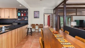 A modern kitchen with wooden cabinets, a black countertop, and a dining area with a long wooden table and chairs. - Foothills Beauty with Pool and Mountain Views (Tucson)