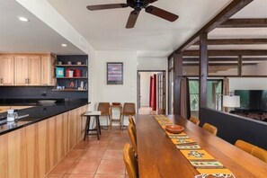 A modern kitchen with wooden cabinets, a black countertop, and a dining area with a long wooden table and chairs.