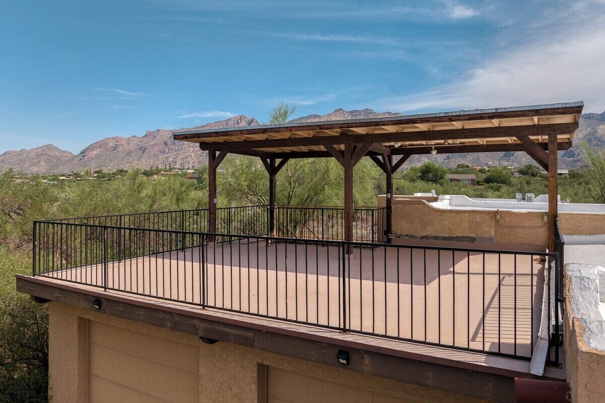 A covered outdoor patio with a metal railing, a concrete floor, and a view of mountains in the background.