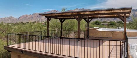 A covered outdoor patio with a metal railing, a concrete floor, and a view of mountains in the background.