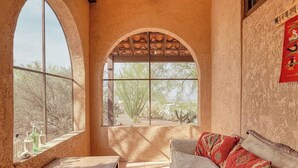 A room with a large arched window, a sofa, and a small table. - Foothills Beauty with Pool and Mountain Views (Tucson)