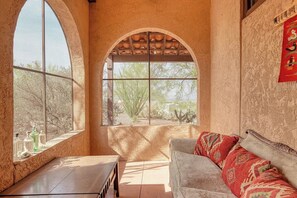 A room with a large arched window, a sofa, and a small table. - Foothills Beauty with Pool and Mountain Views (Tucson)