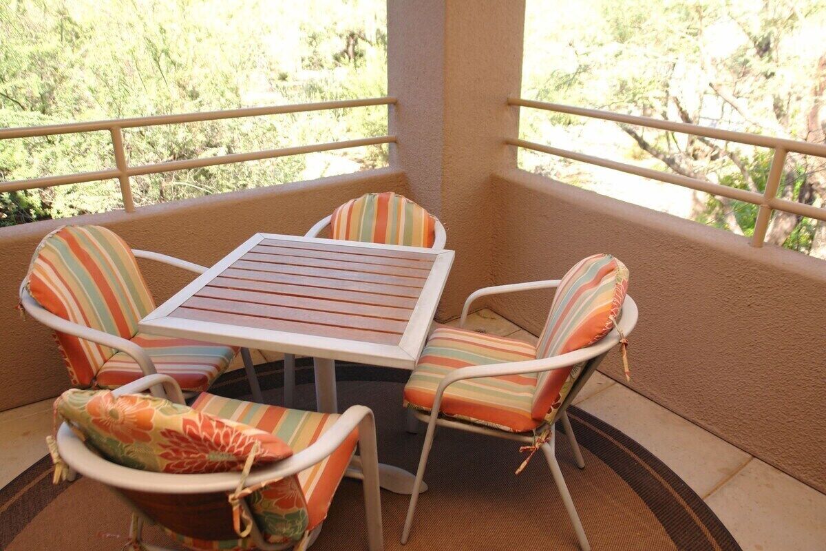 Ein Balkon mit einem Tisch und vier Stühlen, jeweils mit gestreiften Kissen.