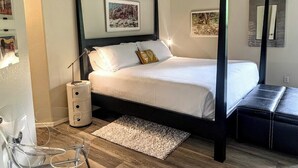 Una cama con dosel, colchón y almohadas blancos, una mesita de noche con lámpara y una pequeña alfombra en el suelo.