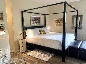Ein Bett mit Baldachin, eine weiße Matratze und Kissen, ein Nachttisch mit Lampe und ein kleiner Teppich auf dem Boden.