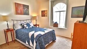 Een slaapkamer met een bed, nachtkastjes, een raam met uitzicht en kunstwerken aan de muren.
