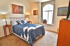 A bedroom with a bed, bedside tables, a window with a view, and artwork on the walls.