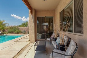 Un patio con piscina, una puerta de cristal que da a una habitación y mobiliario de exterior.