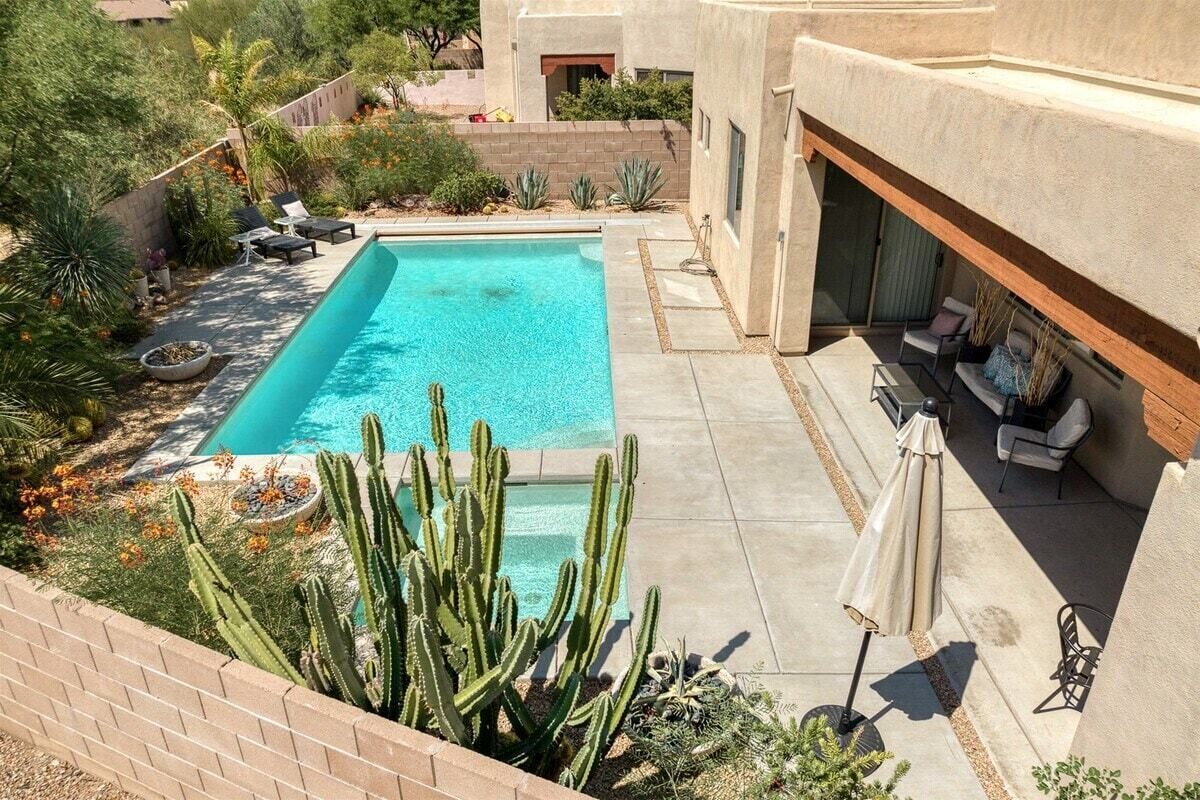 Une piscine avec un espace patio, entourée de cactus et de plantes du désert.