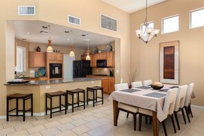 A spacious kitchen with wooden cabinets, a central island, and a dining area with a table and chairs. - Painted Feather - Modern Beauty with Pool and Spa (Tucson)