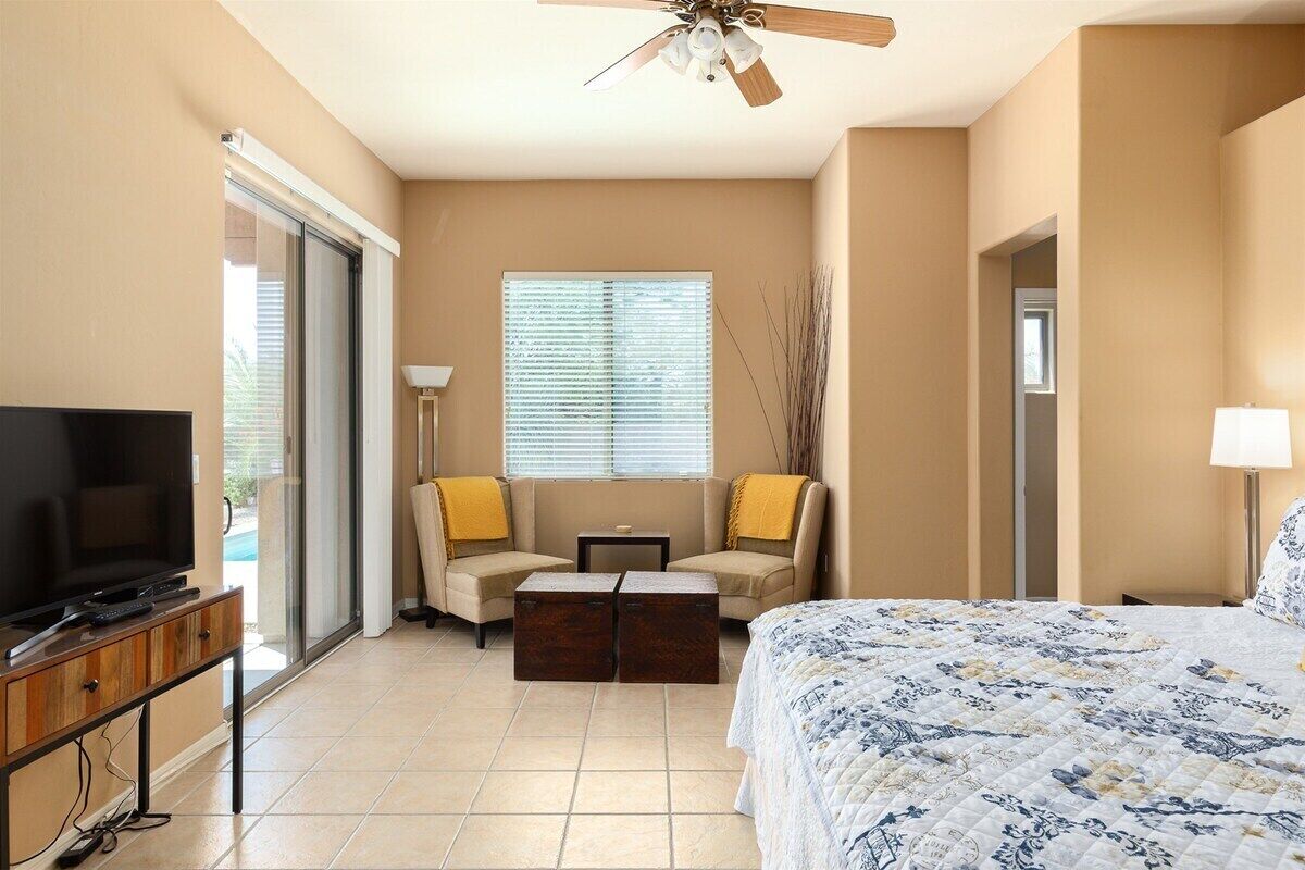 A hotel room with a bed, a television, a sofa, a coffee table, and a window with blinds. - Painted Feather - Modern Beauty with Pool and Spa (Tucson)
