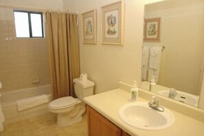 Een badkamer met een badkuip, toilet, wastafel en een grote spiegel.