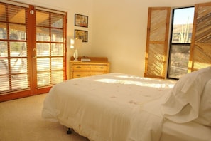 Een slaapkamer met een bed, een houten dressoir en een raam met zonwering.