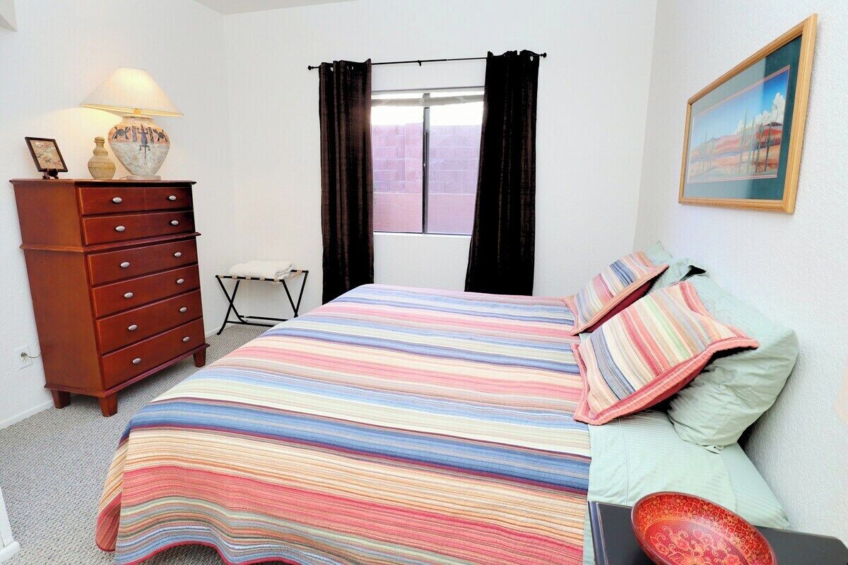 Un dormitorio con cama, cómoda, ventana con cortinas y un cuadro en la pared.