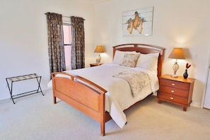 A bedroom with a wooden bed, two bedside tables with lamps, a bench, and a window with curtains.
