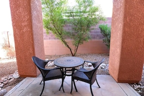 A patio with a round table and four chairs, surrounded by a textured wall and a small tree. - Condo 1111 at Ventana Vista (Tucson)