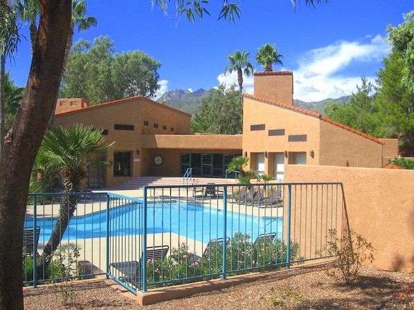 A pool area with a fenced pool, lounge chairs, and a building with a flat roof. - Condo 1111 at Ventana Vista (Tucson)