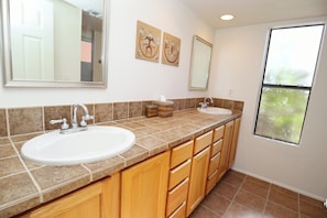 A bathroom with two sinks, wooden cabinets, a mirror, and artwork on the wall.