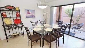 Zona de menjador amb taula de vidre envoltada de cadires, prestatge metàl·lic amb plats i una finestra gran amb vista a l'exterior.