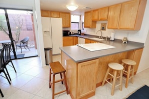 A kitchen with wooden cabinets, a central island with stools, a refrigerator, and a dining area with chairs. - Condo 1111 at Ventana Vista (Tucson)
