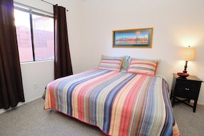 A bedroom with a bed, a window with curtains, a wall-mounted painting, and a bedside table with a lamp. - Condo 1111 at Ventana Vista (Tucson)
