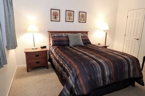 A bedroom with a bed, two bedside tables, lamps, a door, and three framed pictures on the wall. - Ventana Vista 1179 Condo (Tucson)