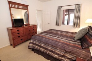 A bedroom with a bed, a dresser, a television, a window with curtains, and a door.