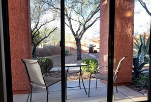 An outdoor patio with two chairs and a table, surrounded by a red textured wall and a view of a tree and landscape. - Ventana Vista 1179 Condo (Tucson)