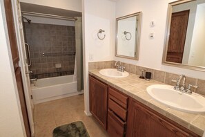 A bathroom with a bathtub, two sinks, wooden cabinets, and a mirror. - Ventana Vista 1179 Condo (Tucson)