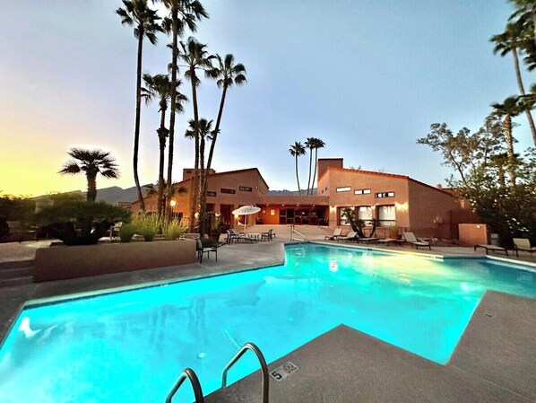 A swimming pool with lounge chairs and palm trees, surrounded by a building with multiple windows. - Condo 1236 at Ventana Vista (Tucson)
