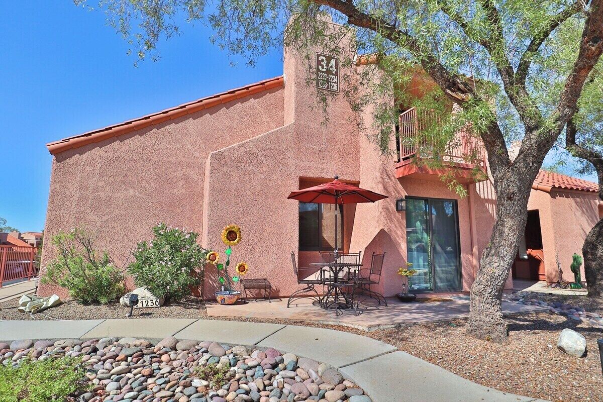A building with a red stucco exterior, a patio with outdoor furniture, and a tree in the foreground.