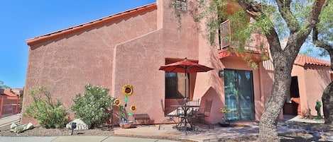 A building with a red stucco exterior, a patio with outdoor furniture, and a tree in the foreground.