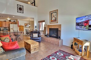 A living room with a fireplace, a television mounted on the wall, and a dining area with chairs and a table. - Condo 1236 at Ventana Vista (Tucson)