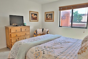 A bedroom with a bed, a wooden dresser, a television, and two framed pictures on the wall.